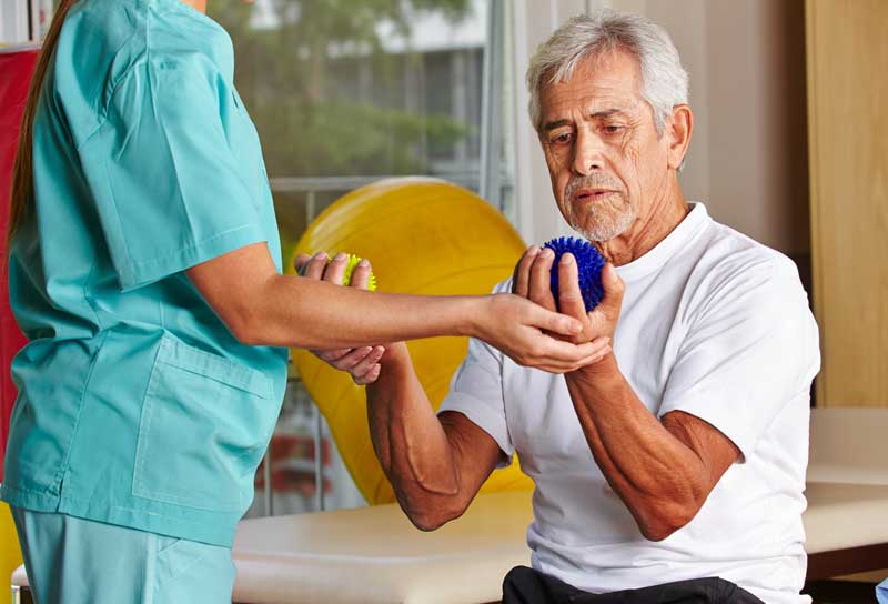 Senior man with spikey balls in gym with physiotherapist.
